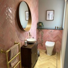 Paris rose brick wall tiles fitted herringbone style in a luxury cloakroom with brass bathroom accesories and feature brass round mirror